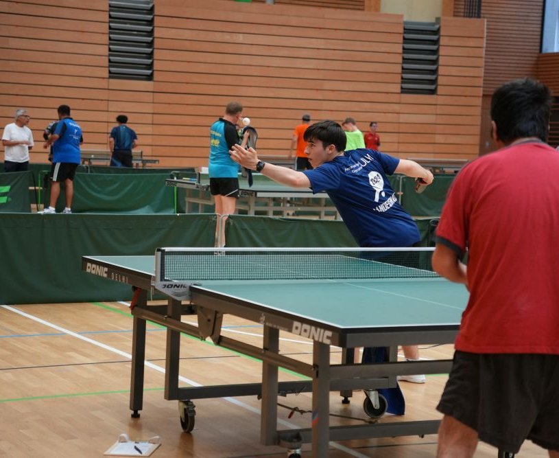 Tischtennisspieler in blau beim Vorhandangriff, Gegner in rotem Shirt