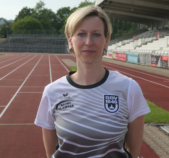 Person in Sporttrikot mit SSV 1846-Logo steht auf roter Laufbahn vor Tribüne