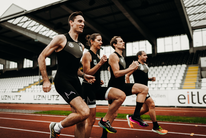 Vier erwachsene Triathletinnen und Triathleten beim Gruppentraining auf Laufbahn