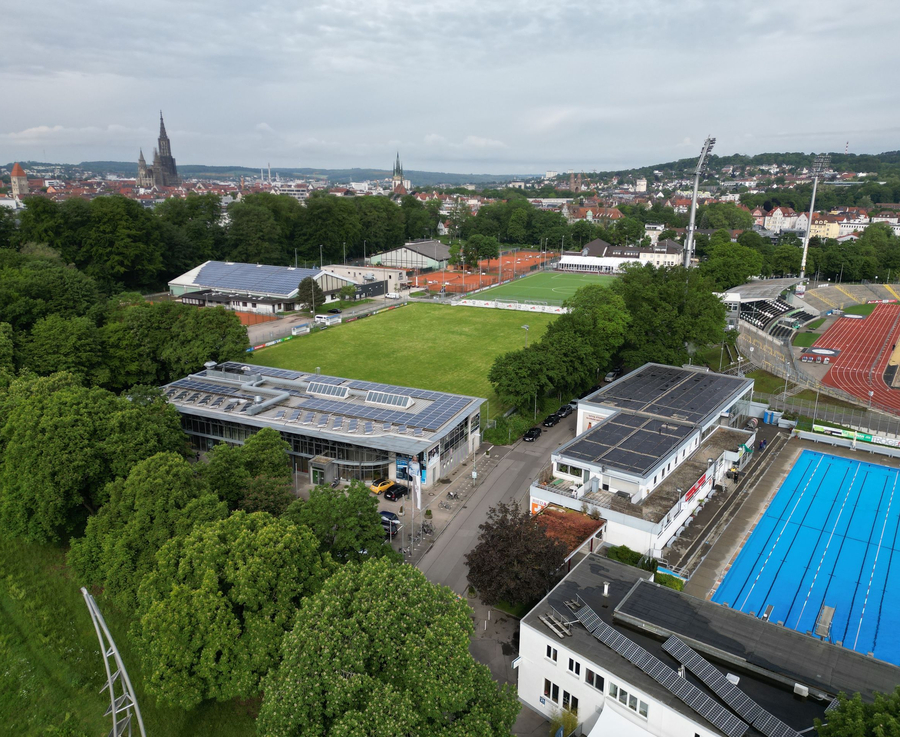 Luftaufnahme Stadiongelände mit Rasenplatz, Tribüne, Parkplätzen und Außen-Schwimmbecken