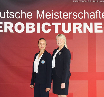 zwei Kampfrichterinnen mit FIG-Lizenz vor Banner Deutsche Meisterschaften Aerobicturnen