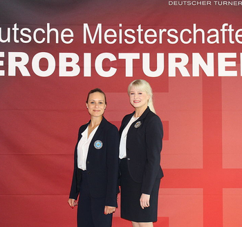 zwei Kampfrichterinnen mit FIG-Lizenz vor Banner Deutsche Meisterschaften Aerobicturnen